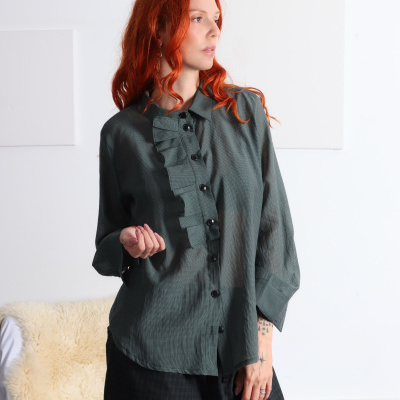 Blusa verde-escuro com folhos frontais e padrão xadrez pequeno usada por mulher ruiva em ambiente interior