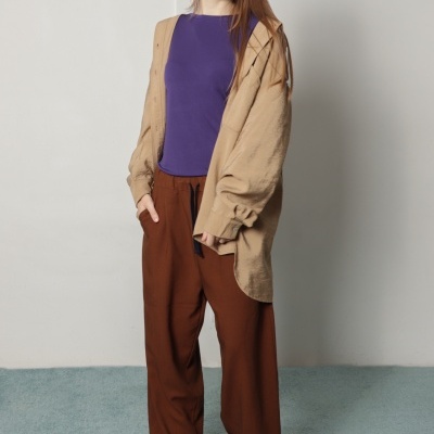 Mulher com camisola roxa, camisa bege aberta e calças castanhas largas