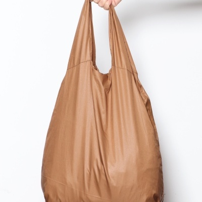 Mala de ombro castanha em tecido sintético com acabamento brilhante segurada por uma mão