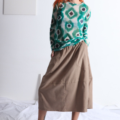 Mulher com camisola estampada verde e saia bege em fundo branco