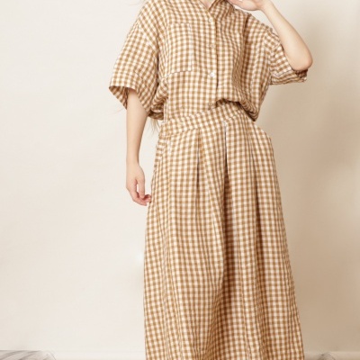 Mulher com conjunto de camisa e saia comprida xadrez bege e branco, sapatos castanhos claros, em fundo neutro