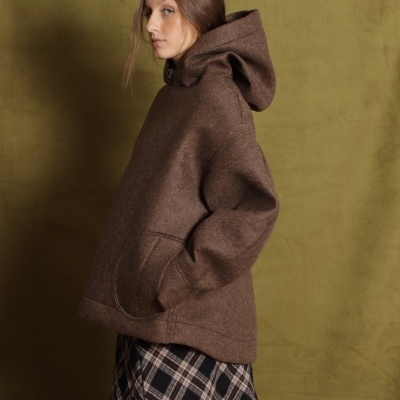 Mulher com casaco castanho e saia xadrez num fundo verde