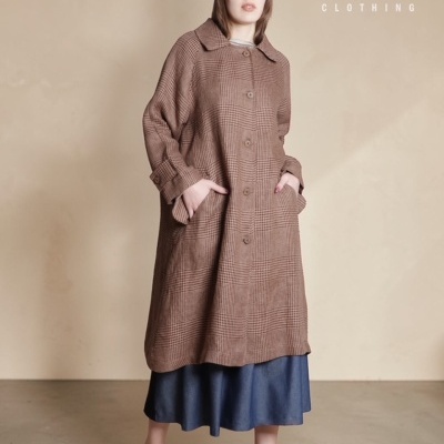 Mulher a usar casaco comprido castanho xadrez com botões e colarinho, saia azul escura e sapatilhas bege