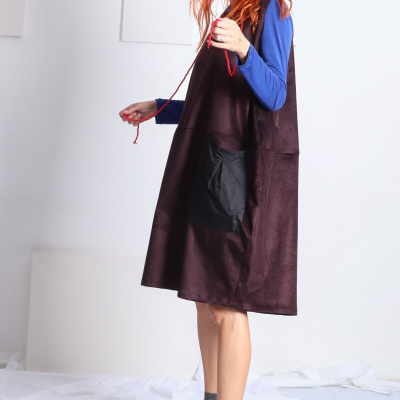 Vestido castanho escuro com bolso preto, mulher com camisa azul, meias cinza e sapatos pretos em fundo branco