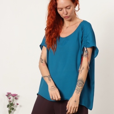 Mulher com blusa azul turquesa de manga curta e calças castanhas escuras