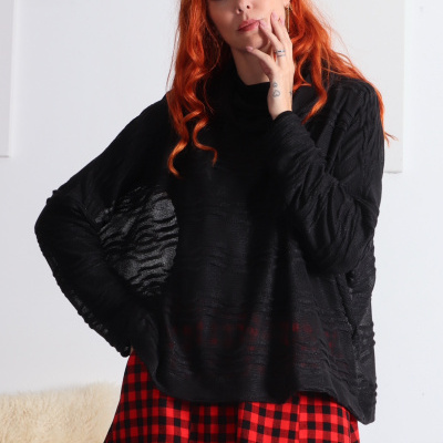 Mulher com camisola preta texturada e saia xadrez vermelho e preto.