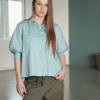 Mulher com camisa azul clara de manga bufante e calças verdes largas