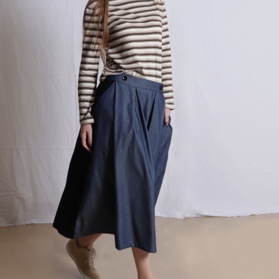 Mulher com camisa às riscas, saia midi azul e ténis bege sobre fundo neutro