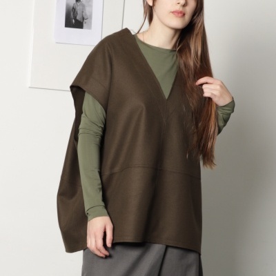 Mulher com camisola castanha, camisa verde e calças cinzas.