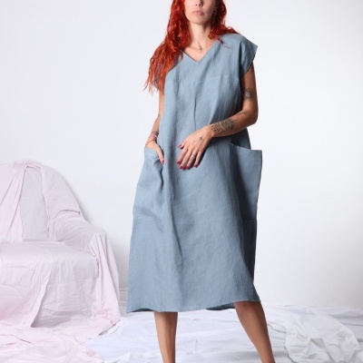 Vestido azul claro de linho com bolsos, mulher ruiva de cabelo solto em fundo branco.
