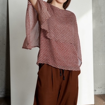 Mulher vestindo blusa rosa com padrão de pontos brancos e calças largas castanhas