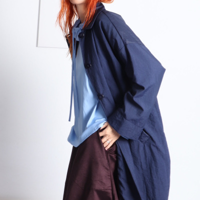 Mulher com casaco azul, blusa azul clara e saia castanha em fundo branco.