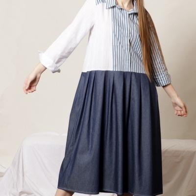 Modelo com vestido comprido azul e branco e ténis brancos em estúdio com fundo neutro.