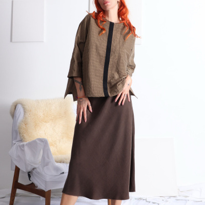 Mulher com camisola castanha e saia castanha num ambiente interior.