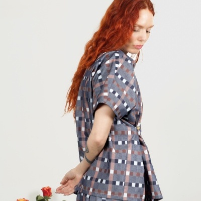 Mulher com roupa xadrez azul, castanho, branco e cinza junto a duas rosas vermelhas e amarelas