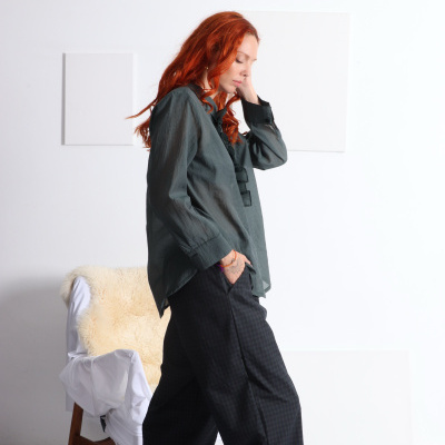 Mulher com blusa cinza escura, calças xadrez escuras, meias vermelhas e sapatos pretos em ambiente branco.