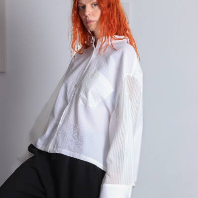 Mulher com blusa branca oversized e calças pretas largas em fundo branco.