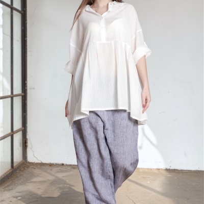 Mulher com blusa branca larga e calças cinza num espaço interior