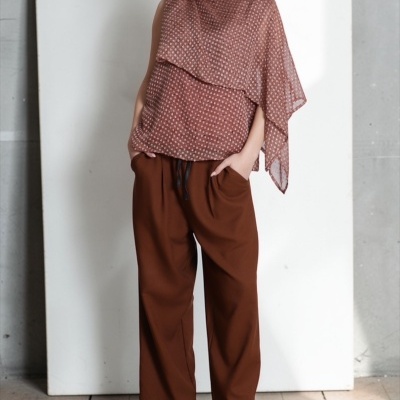 Mulher com blusa castanha com padrão, calças largas castanhas e sandálias castanhas numa sala interior