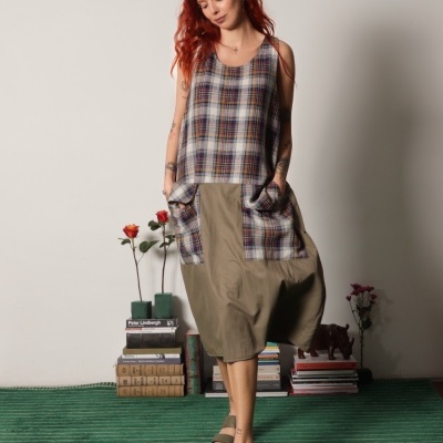 Vestido xadrez e caqui com bolsos, mulher ruiva, sandálias verdes, tapete às riscas, livros e flores ao lado