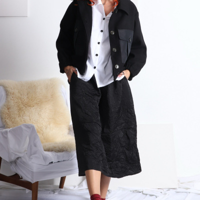 Mulher com casaco preto, camisa branca e saia preta num ambiente interior