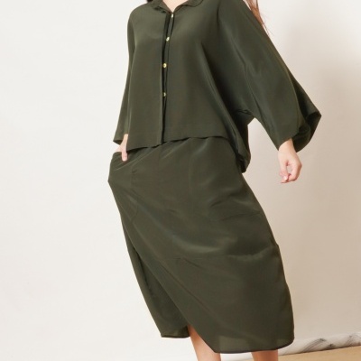 Mulher com conjunto verde-oliva de blusa e saia e sandálias sandálias preto e branco.