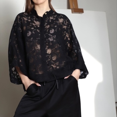 Mulher vestindo blusa preta de renda floral e calças pretas largas em estúdio