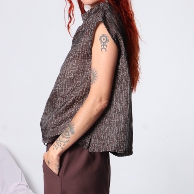 Mulher de perfil com blusa sem mangas em tons castanhos e calças castanhas