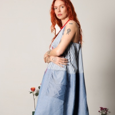 Vestido riscas azuis e brancas com parte inferior azul e bolso, usado por mulher ruiva com tatuagens