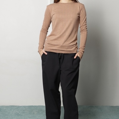 Mulher com camisola castanha de riscas e calças pretas largas em estúdio