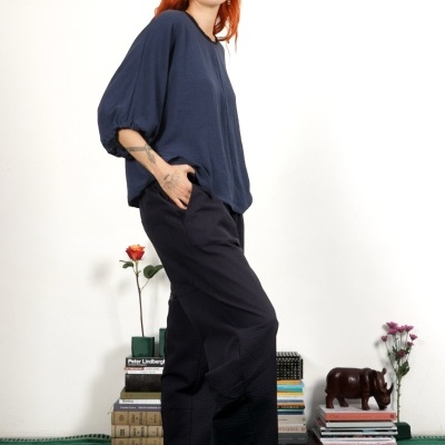 Mulher com vestuário casual azul e preto, sandálias bicolores, sobre tapete verde com elementos decorativos e livros
