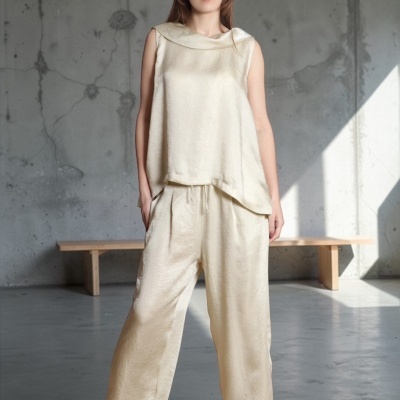 Macacão creme acetinado com top e calças largas usado por mulher com sandálias pretas em ambiente industrial.