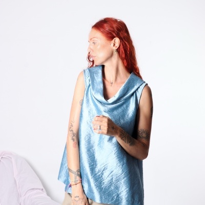 Mulher com blusa azul claro de tecido sedoso e calças bege em fundo branco
