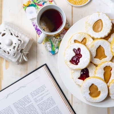 Biscoitos decorados em formas de coelho, sino e cenoura com chá numa mesa branca.