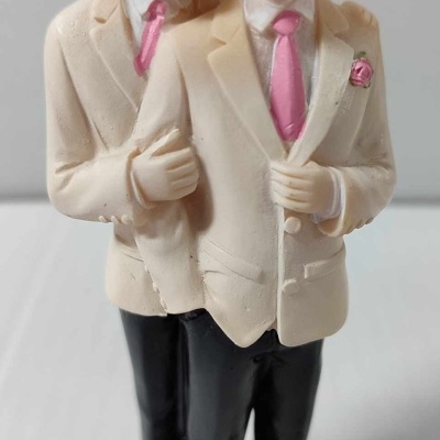 Figurine de dois homens com fatos creme e gravatas rosa, sobre base com flores amarelas