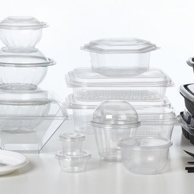 Conjunto de embalagens plásticas transparentes e pretas com talheres e copos, sobre superfície branca