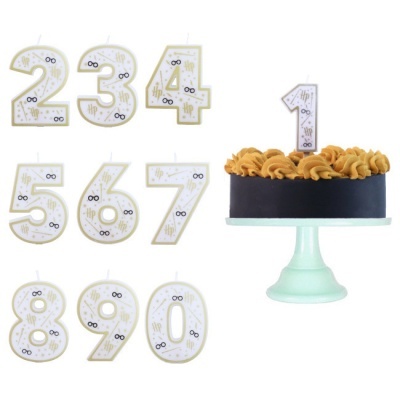 Velas de aniversário em números com design de óculos e símbolos dourados ao lado de bolo com vela número 1 acesa em suporte verde claro.
