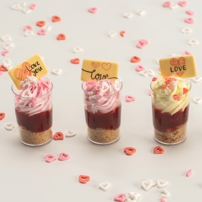 Três sobremesas em copos transparentes decoradas com chantilly e placas de chocolate com mensagens de amor
