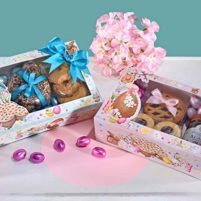 Caixas de presentes com biscoitos, chocolates e ovos de Páscoa embalados com fitas, decorados com flores cor-de-rosa em fundo verde-azulado.