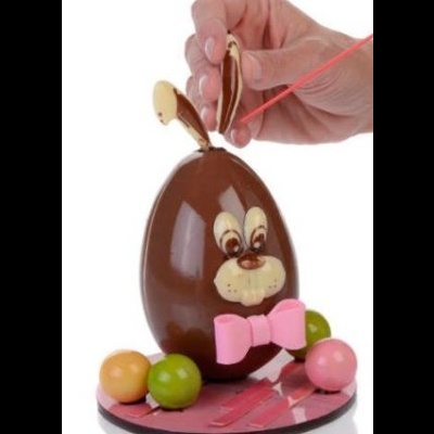 Ovo de chocolate em forma de coelho com laço rosa e bolas de chocolate coloridas ao redor