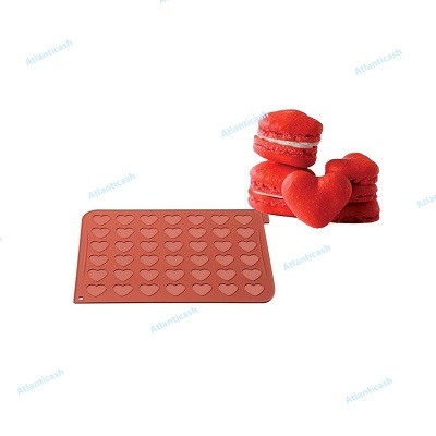 Tapete de silicone vermelho com cavidades em forma de coração ao lado de macarons vermelhos em forma de coração.