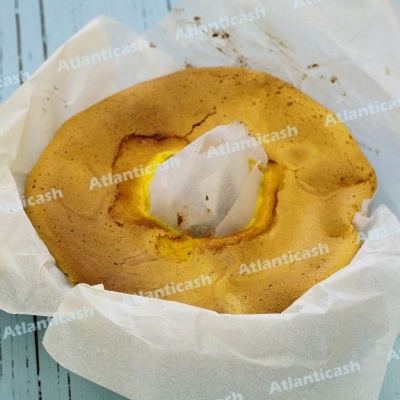 Bolo redondo dourado com papel vegetal branco sobre superfície de madeira azul claro
