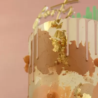 Bolo decorado em bege, branco e dourado com folhas douradas e detalhes em rosa