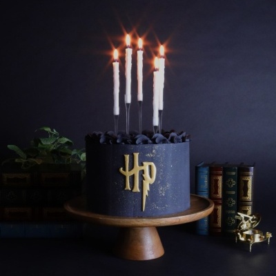 Bolo azul escuro decorado com símbolo dourado HP e velas acesas num suporte de madeira