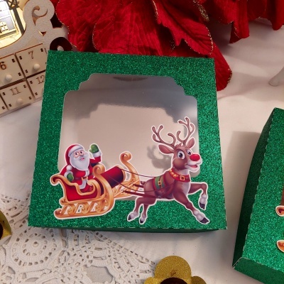 Caixa verde com glitter e ilustração de Pai Natal no trenó com rena