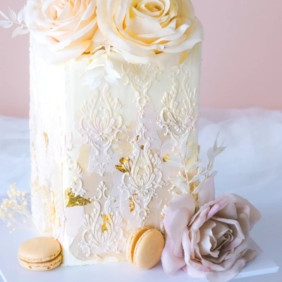 Bolo branco decorado com rendilhado dourado e flores artificiais com macarons.