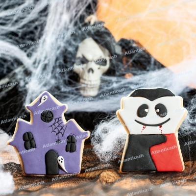 Biscoitos decorados de Halloween em forma de casa assombrada e vampiro, sobre fundo com teias de aranha e caveira