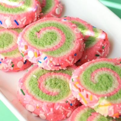 Biscoitos em espiral verde e rosa com confeitos coloridos num prato branco