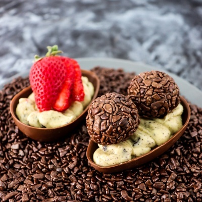 Dois ovos de chocolate recheados com creme e decorados com morango e brigadeiros