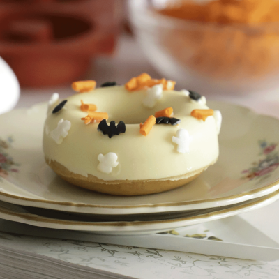 Donut com glacê branco e confeitos de Halloween em prato branco com bordas douradas